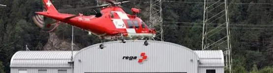Roter Helikopter in der Luft vor Rega-Gebäude