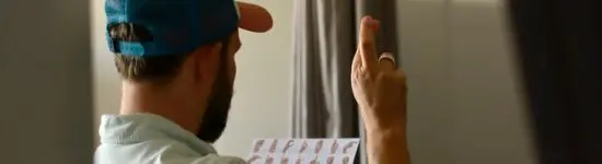 Ein Mann schaut auf ein Blatt mit dem DSGS-Alphabet und gebärdet den Buchstaben "R".