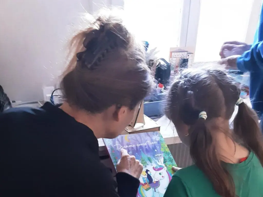 Man sieht eine Frau und ein Mädchen von hinten und sie schauen zusammen ein Bild mit einem Einhorn an.