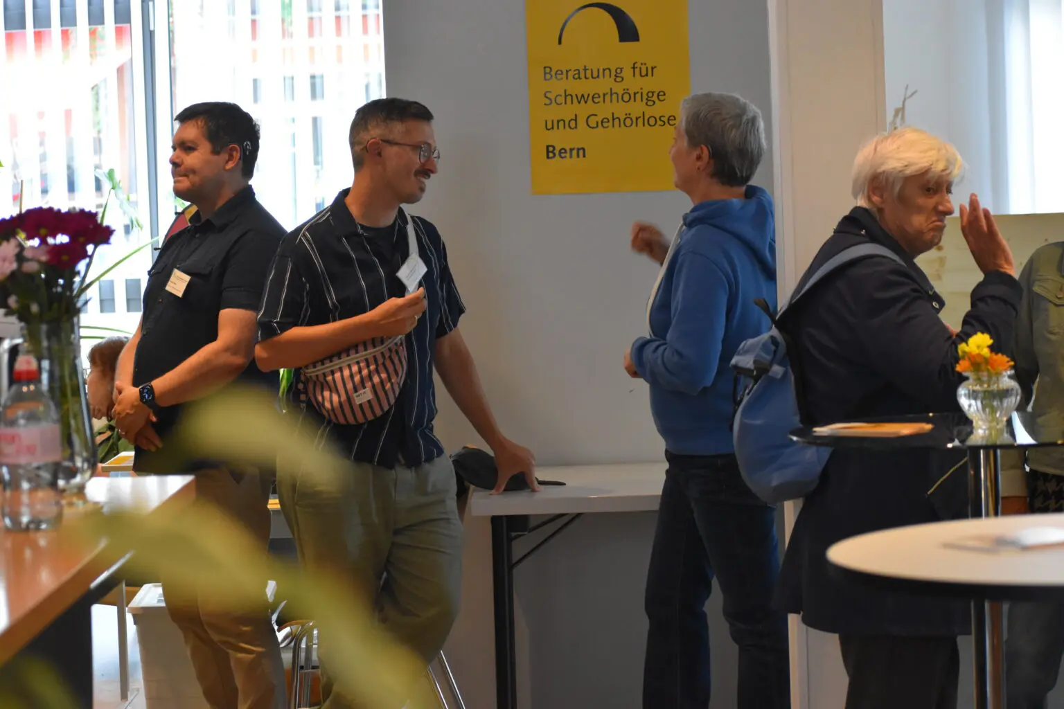 Open House & Sommerfest BFSUG Bern. 4 Personen auf dem Bild die sich austauschen. in Lautsprache und Gebärdensprache.