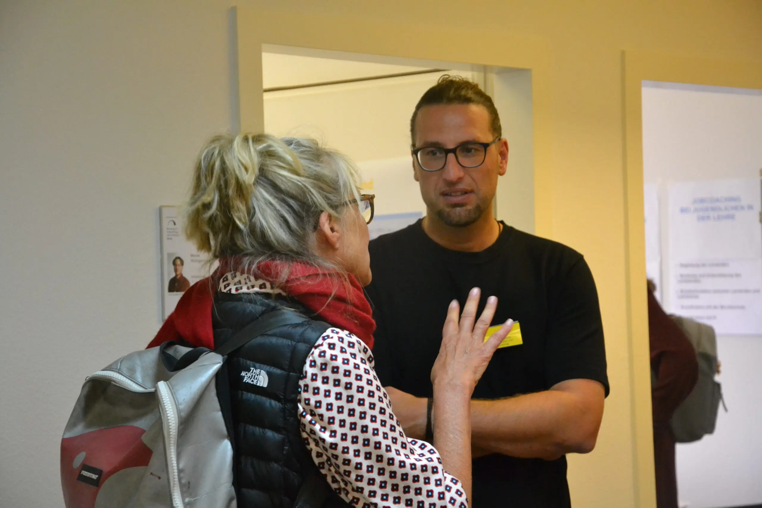 Zwei Personen sprechen miteinander. Die eine Person steht mit dem Rücken zur Kamera und die andere Person hört ihr zu.