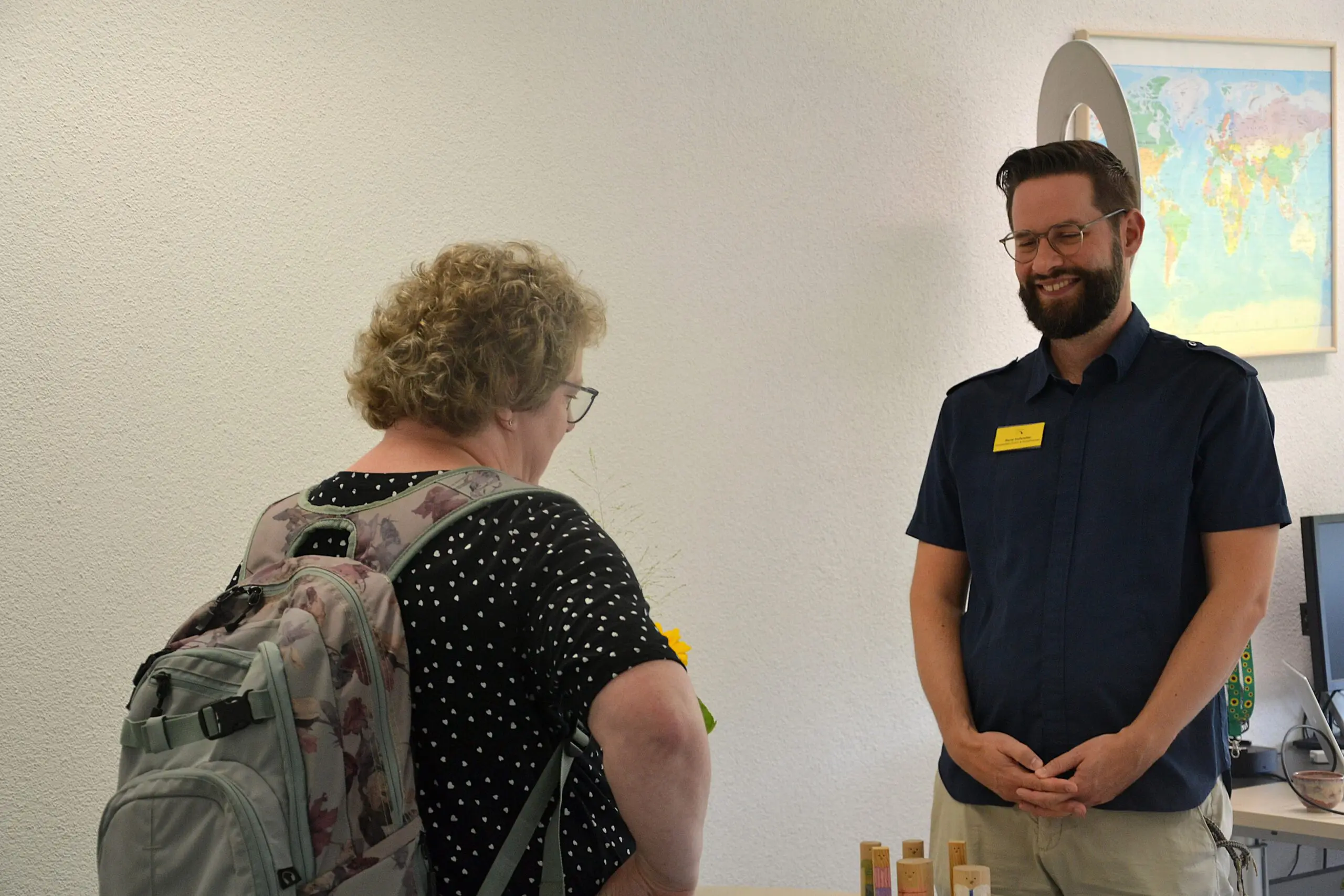 Zwei Personen stehen sich gegenüber. Die eine Person steht mit dem Rücken zur Kamera. Die andere Person lächelt.