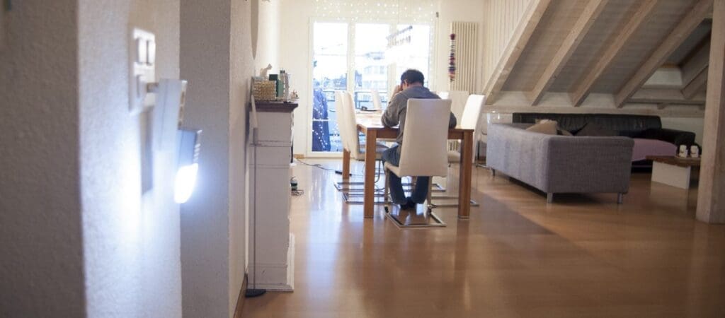 Ein Mann sitzt in einer hellen Wohnung an einem Tisch mit seinem Kopf auf seine Hand gestützt.