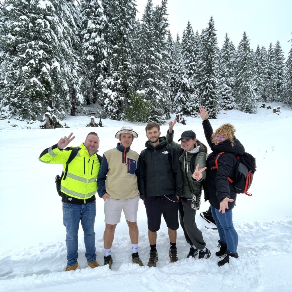 Fünf Personen stehen in einer verschneiten Landschaft nebeneinander und lächeln in die Kamera.